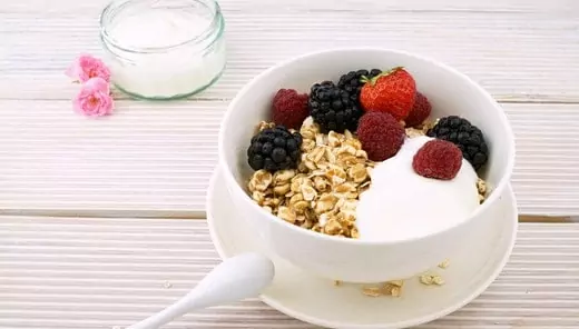 A full white bowl consists of blueberries, strawberries, and red-berried with oats and maple syrup.