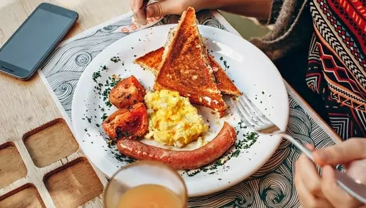 a girl eating mexican scrambled eggs with a sandwich, sausage with help of a fork. a traditional breakfast recipe starts with m in the usa.