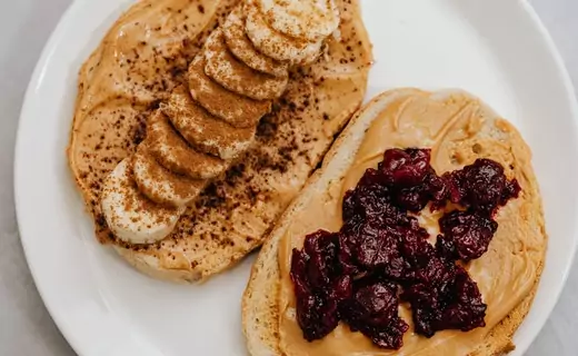 the plate contain bread spread with peanut butter and fruits like apple, bananas